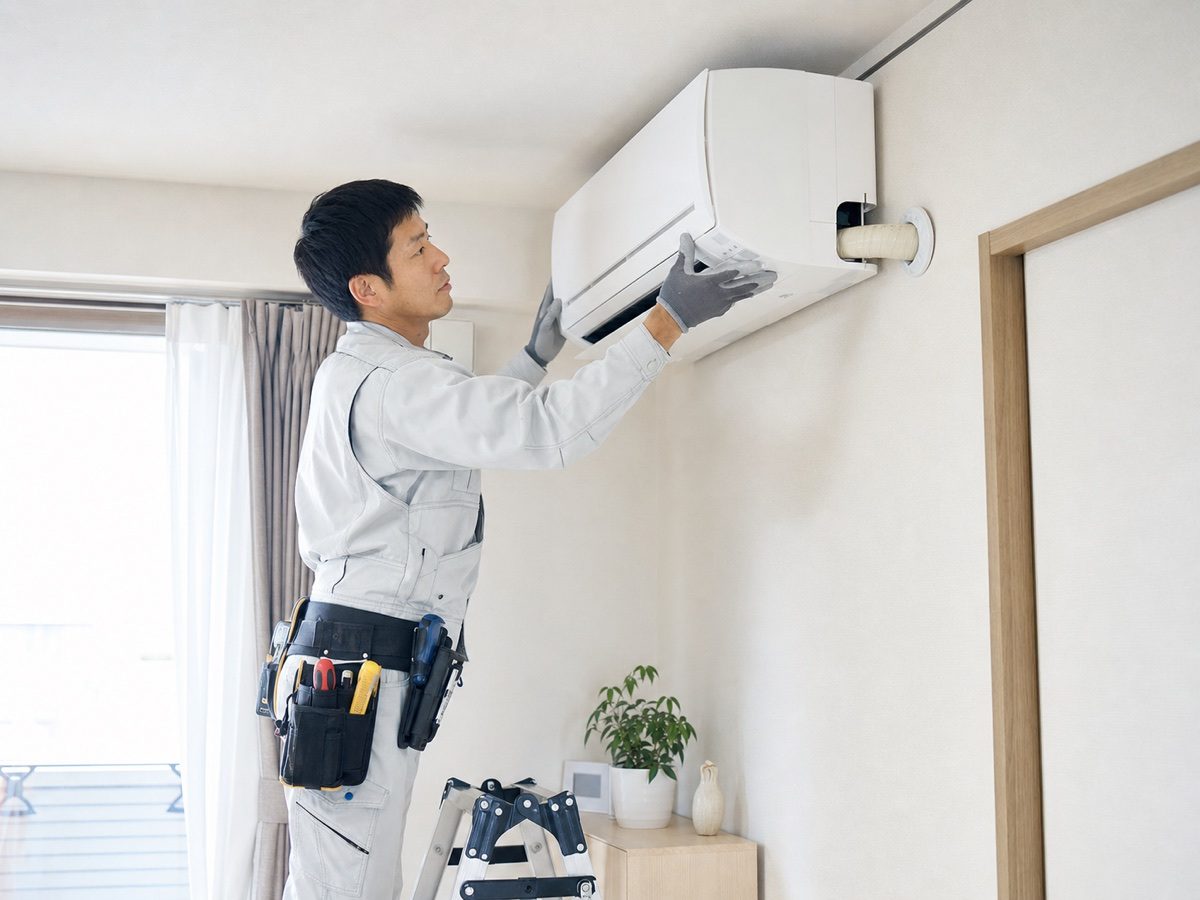 住宅の壁掛けエアコンを点検する職人(AI・構成見本)
