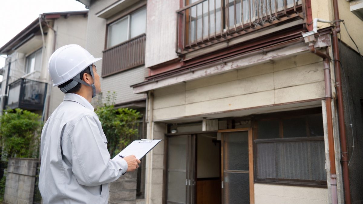二階建て住宅の前で図面を見ながら現地確認する人物(AI・構成見本)