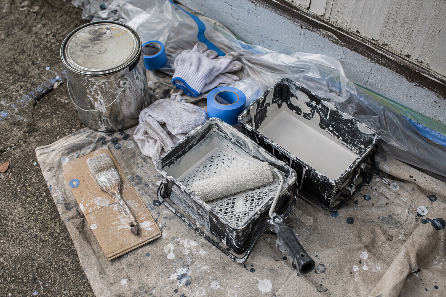 Used paint trays, brushes, and tape on a protected work surface — illustrative image